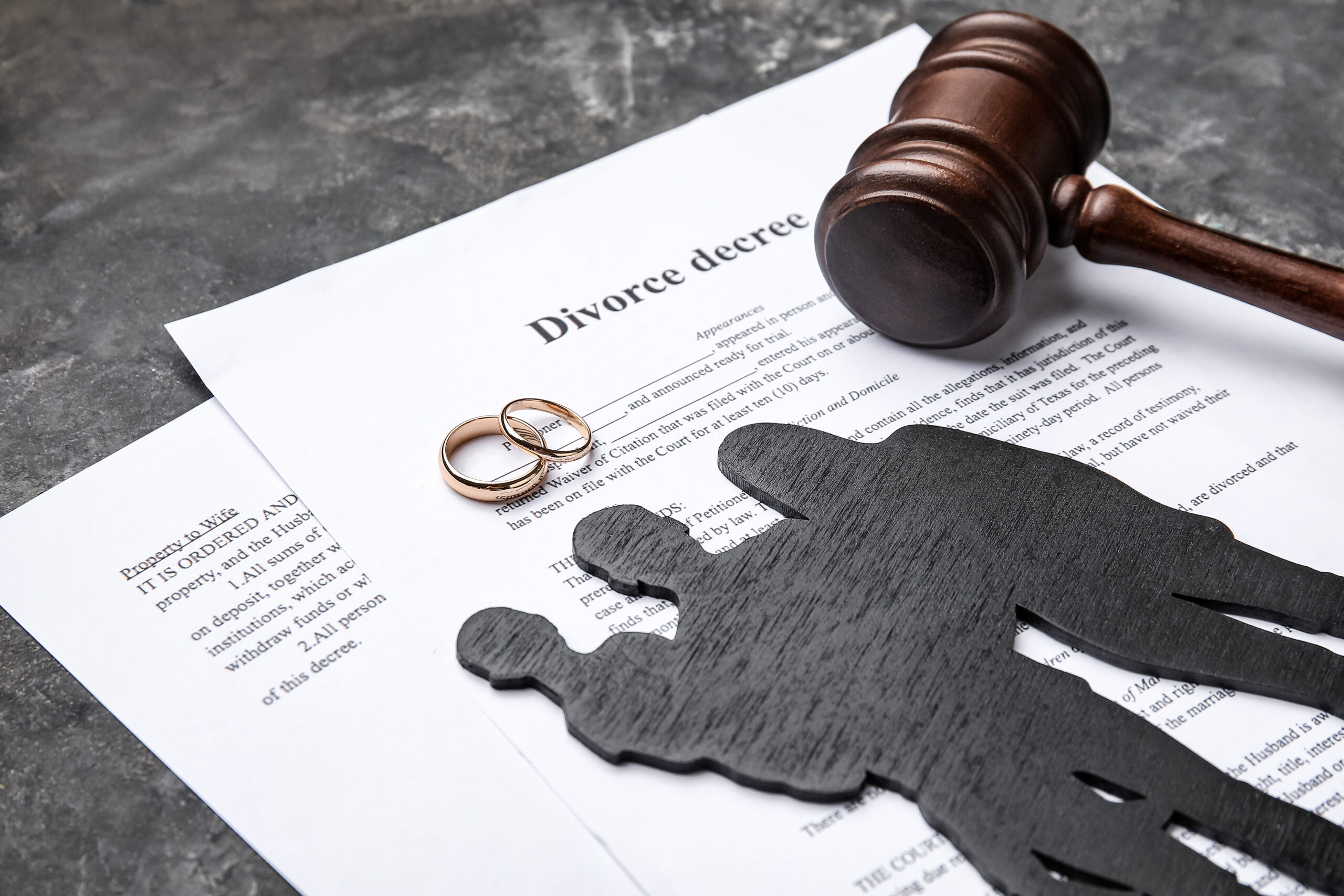  A black figure of family, judge's gavel, and rings placed on the divorce decree. 